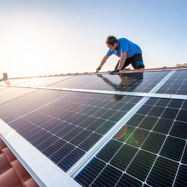 kneeling professional fixing solar panels from the top of a house roof