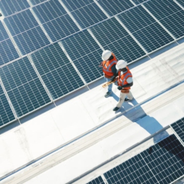 An aerial view of solar panels over the roof & two workers walking in the middle space at Ocala, FL.